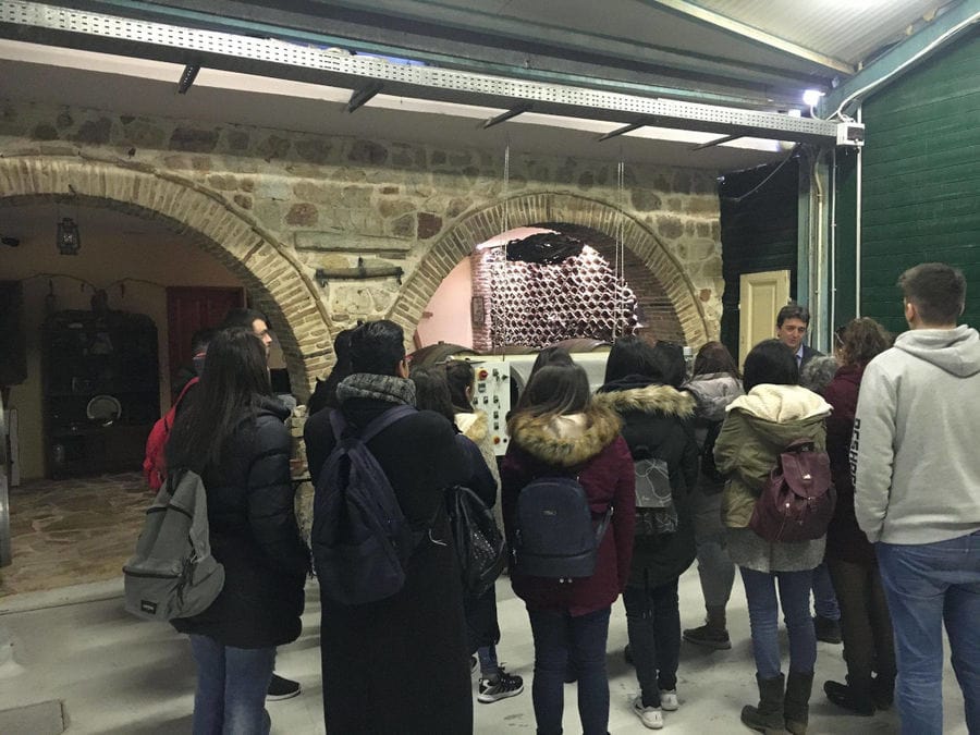 guide presenting young visitors the Nikolou Winery plant in front of grape press machine